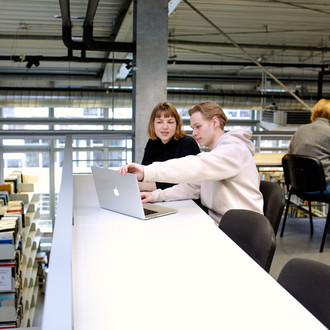 Mehrere Studierende sitzen an Tischen in der Bibliothek und arbeiten.
