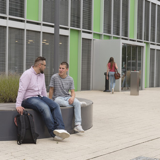 Studierende sitzen vor einem Gebäude.