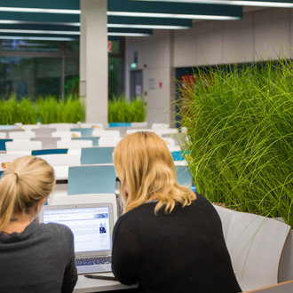 Zwei Studentinnen sitzen mit einem Laptop an einem Tisch.