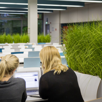 Zwei Studentinnen sitzen mit einem Laptop an einem Tisch.