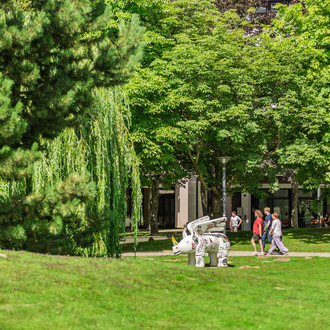 Studierende auf dem grünen Campus mit Nashornskulptur