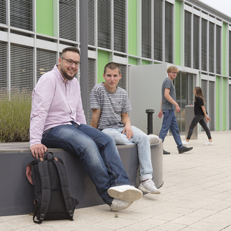 Studierende sitzen vor einem Gebäude.