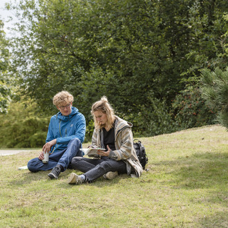 Zwei Studierende sitzen auf einer Wiese.