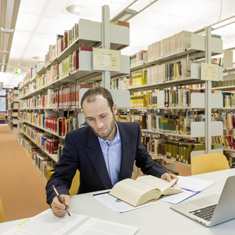 Ein Studierender sitzt lernend an einem Arbeitsplatz in der Bibliothek.