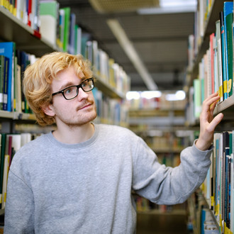 Studierender steht suchend an einem Bücherregal in der Bibliothek.