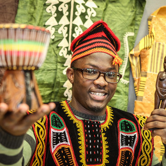 Ein internationaler Studierender in traditioneller afrikanischer Kleidung lächelt in die Kamera.