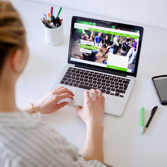 Am Schreibtisch sitzende Studentin tippt auf dem Laptop, daneben liegen Bücher und Stifte.