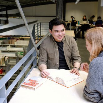 Zwei Studierende sitzen an einem Arbeitsplatz in der Bibliothek und lesen.