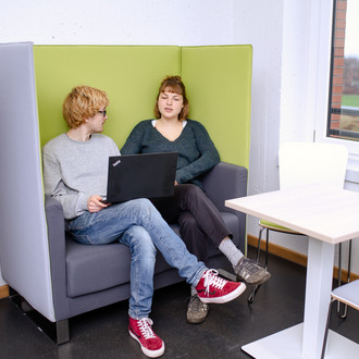 Zwei Studierende sitzen auf einem Sessel und unterhalten sich miteinander.