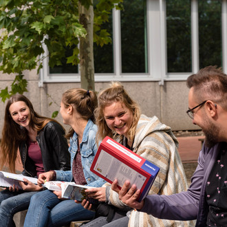 Vier Studierende sitzen auf einer Bank und unterhalten sich.